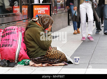 Stockholm, Schweden, 24. Juni 2014: Eine unbekannte Frau sitzt ruhig und Bitten um Geld mit einem Becher vor ihr auf Drottninggatan. Stockfoto