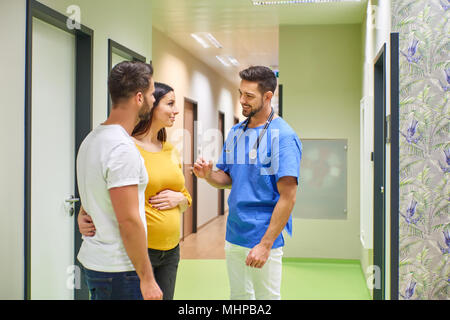 Ein schöner männlicher Arzt Beratung mit einem jungen schwangeren Paare beim Stehen in den Krankenhäusern Flur. Stockfoto