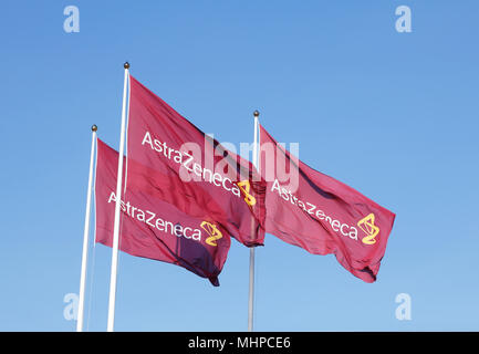 Södertälje, Schweden - 27. April 2014: Drei lila Fahnen mit dem Logo für Atrazeneca im Wind fliegen auf der Oberseite der Fahnenmasten gegen den blauen Himmel. Stockfoto