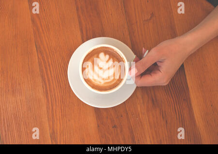 Die junge Dame, mit wunderschönen Maniküre Holding eine Tasse Cappuccino und Latte Kunst auf hölzernen Tisch in einem Cafe. Stockfoto