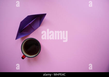 Papier Schiff, eine Tasse Kaffee am Morgen auf Pastell violett unterlegt mit Text. Stockfoto
