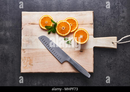 Flach von frischen Zitrusfrüchten, die Hälfte Orangenscheiben auf Schneidebrett mit Messer an schwarzen Stein Hintergrund. Horizontale Ansicht von oben. Stockfoto