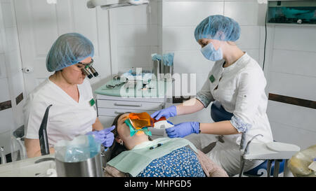 Frau beim Zahnarzt Klinik erhält der zahnmedizinischen Behandlung ein Loch in einen Zahn zu füllen. Zahnersatz und Verbundmaterial Polymerisation mit UV-Licht und Laser. Stockfoto