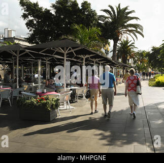 Drei Menschen zu Fuß hinter einem Cafe auf der Promenade in Funchal, der Hauptstadt von Madeira Stockfoto