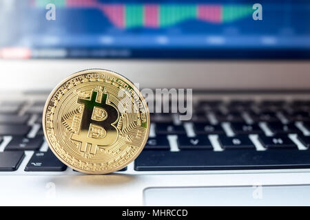 Physische Bitcoin auf Laptop mit Charts auf dem Bildschirm platziert Stockfoto
