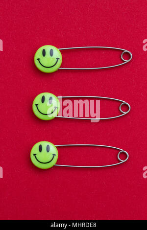 Kunststoff Kopf metall Sicherheitsnadeln auf rotem Papier festgesteckt. Leichte frische grüne Lächeln emoticon Safety Pin. Nett und lustig bunte Emoticons. Stockfoto