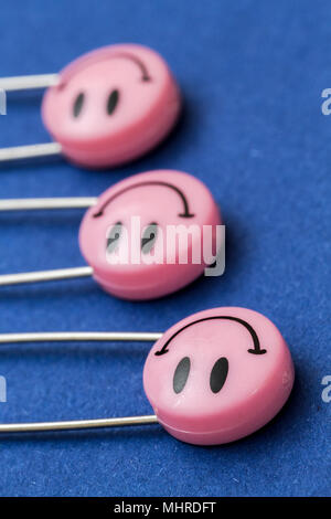 Kunststoff Kopf metall Sicherheitsnadeln in Papier festgesteckt. Rosa Lächeln emoticon Safety Pin. Nett und lustig bunte Emoticons. Stockfoto