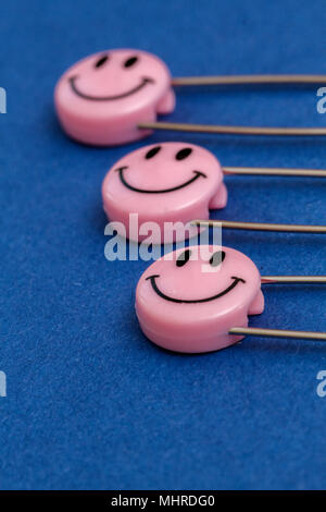 Kunststoff Kopf metall Sicherheitsnadeln in Papier festgesteckt. Rosa Lächeln emoticon Safety Pin. Nett und lustig bunte Emoticons. Stockfoto