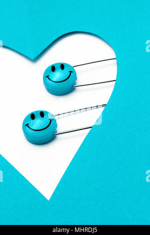 Kunststoff Kopf metall Sicherheitsnadeln in Herzform Papier festgesteckt. Blau Cyan Lächeln emoticon Safety Pin. Nett und lustig bunte Emoticons. Stockfoto