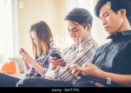 Gruppe junger Geschäftsmann, sitzen auf dem Sofa halten sich an den Händen und mit Hilfe von digitalen Smartphone, Tablet, Coworking team konzept, verschwommenen Hintergrund Stockfoto