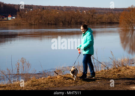 Frau mit einem Hund Spaziergänge am Flussufer an einem Frühlingstag. Freizeitaktivitäten. Stockfoto
