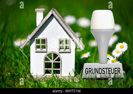 Miniaturhaus im Gras- und Vermögenssteuer Stempel Stockfoto