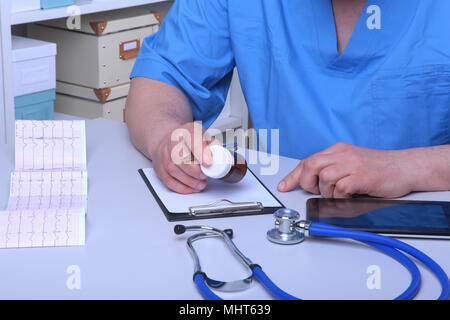 Der Arzt hält einen Blister mit Pillen in die Hand und schreibt die Verordnung in den Arbeitsplatz hautnah. Arzneimittel verschreiben, eine zugelassene Apotheke, Behandlung von Krankheiten Stockfoto