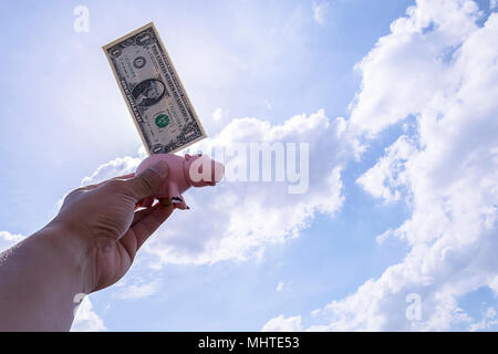 Ein sparschwein mit einem Griff in den Himmel gehalten, gibt es einen Dollar gesteckt, die Kulisse ist ein helles und hellen Himmel, Big cloud White Stockfoto