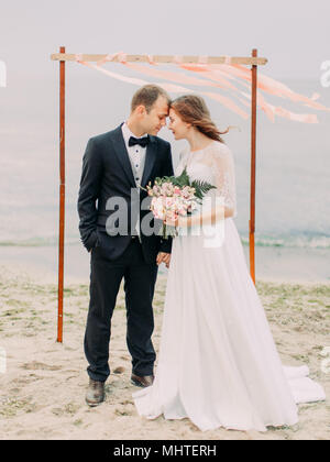In voller Länge ansehen Der Jungvermählten ständigen Kopf-an-Kopf am Strand. Stockfoto