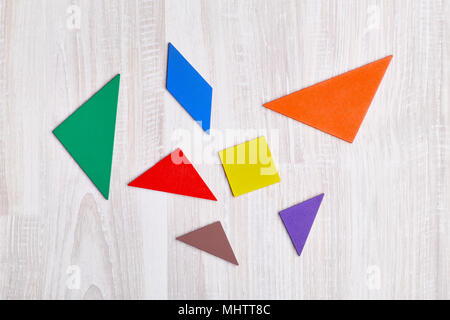 Farbige geometrische Stücke von Puzzle wie Dreiecke, Quadrat, Parallelogramm, sind auf einem hellen Hintergrund verstreut Stockfoto