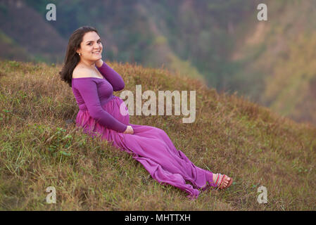 Lächelnd schwangere Frau draußen sitzen auf Gras Stockfoto