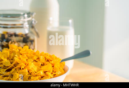 Schüssel Müsli mit Löffel auf Holz Tisch in der Nähe Müsli in Glas Behälter legen und ein Glas Milch. Calcium essen Frühstück für Kinder, bevor sie auf sc Stockfoto