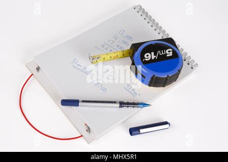 Notizblock, Stift und Maßband mit Arbeiten gekritzelte Notizen, Schuß auf einen weißen Hintergrund, mit einem Schlagschatten. Stockfoto