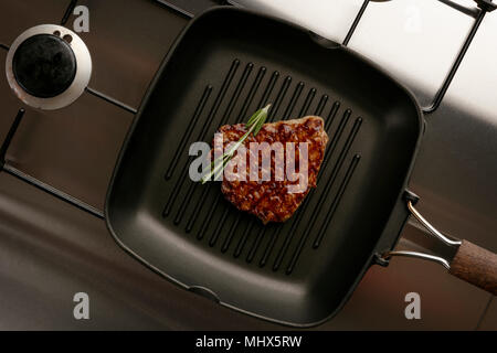 Frische leckere Steak braten in einer Bratpfanne Pfanne mit einem Zweig Rosmarin, auf einem Edelstahl Kochfeld. Stockfoto