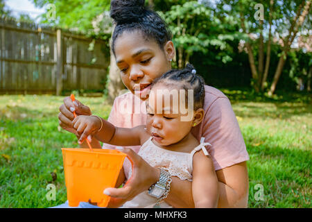 Mitte der erwachsenen Frau spielen mit Spielzeug Eimer in Garten mit Tochter Stockfoto