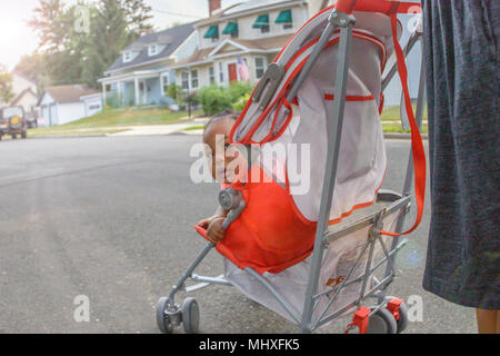 Baby Mädchen in Kinderwagen schaut über ihre Schulter auf suburban Bürgersteig, Porträt Stockfoto