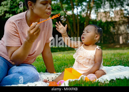 Mitte der erwachsenen Frau Blasen Blasen im Garten für Baby Tochter Stockfoto