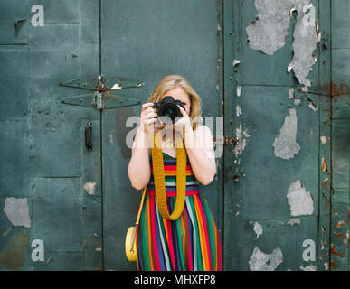 Junge Frau im gestreiften Kleid vor der industriellen Tür Fotografieren, Portrait Stockfoto
