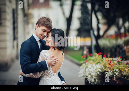 Bräutigam zärtlich umarmen asiatische Braut im weißen Kleid Stockfoto