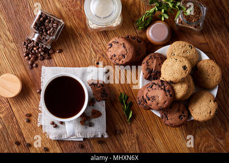 Konzeptionelle Zusammensetzung mit umgestürzten Glas Glas der Kaffeebohnen, transparente Flasche Instant Kaffee und leckere Chocolate Chip Cookies auf Holz- Tabl Stockfoto