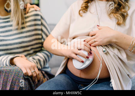 Schwangere Frau und Freund auf dem Sofa mit pränatalen Abhörgerät, 7/8 Stockfoto