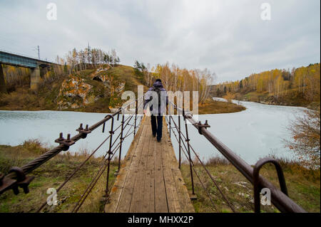 Ansicht der Rückseite des jungen männlichen Wanderer zu Fuß über den Fluss Fußgängerbrücke, Kislokan, Evenk, Russland Stockfoto