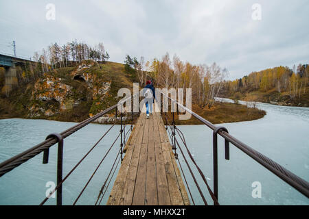 Ansicht der Rückseite des kleinen Gruppe Wanderer zu Fuß über den Fluss Fußgängerbrücke, Kislokan, Evenk, Russland Stockfoto