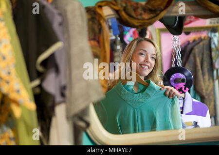 Spiegelbild der jungen Frau, die versucht, auf Vintage Kleidung in Sparsamkeitspeicher Stockfoto