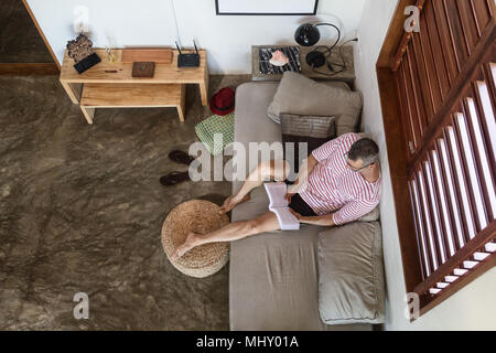 Reifer Mann auf dem Sofa lesen Buch, Ansicht von oben Stockfoto