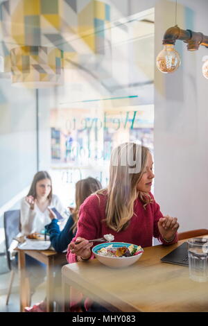 Frau isst Müsli im Cafe, mit Laptop Stockfoto