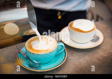 Barista gießen schaumigen Milch in die Kaffeetasse, close-up Stockfoto