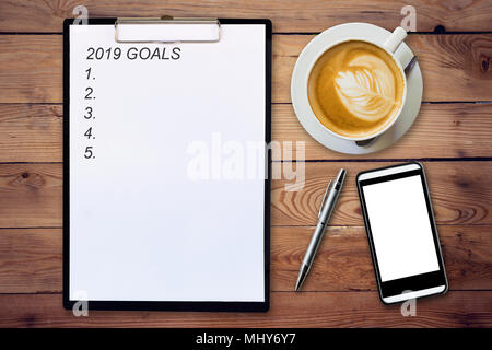 Blick von oben auf die Zwischenablage geschrieben Ziele 2019 auf hölzernen Hintergrund mit Kaffeetasse, Pen und Handy. Stockfoto