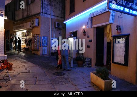 Touristen, die auf der Suche an einem Baugruppenträger oat ein Geschenk Shop in einer schmalen Straße, die Rue Georges Clemenceau in der alten Stadt, Calvi auf Korsika, einer französischen Insel im Sou Stockfoto