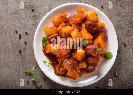 Kartoffeln Eintopf mit Schweinefleisch Wurstscheiben und Tomatensauce auf einem weißen Teller - Ansicht von oben Stockfoto