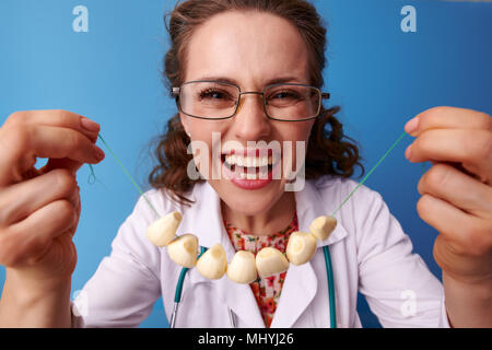 Lächelnd Kinderarzt Frau in Weißem medizinischen Robe mit Knoblauch Perlen auf blauem Hintergrund Stockfoto