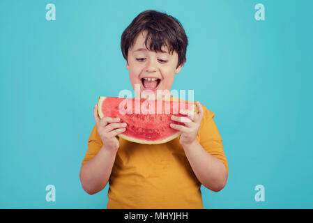 Glückliches Kind isst Wassermelone auf blauem Hintergrund glückliches Kind isst Wassermelone auf blauem Hintergrund Stockfoto