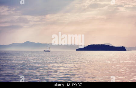 Ein minimalistisches und dramatischen Blick auf einer Yacht auf dem Weg zu einer Insel auf dem offenen Meer unter einem versilberung Sky Stockfoto