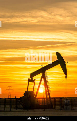 Pumpjack und Sendetürme bei Sonnenuntergang symbolisieren ökologischen Übergang. Eine Pumpenbuchse mit Strommasten und Stromleitung gegen einen roten Himmel. Stockfoto