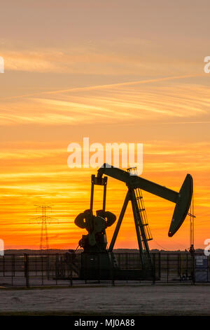 Pumpjack und Sendetürme bei Sonnenuntergang symbolisieren ökologischen Übergang. Eine Pumpenbuchse mit Strommasten und Stromleitung gegen einen roten Himmel. Stockfoto