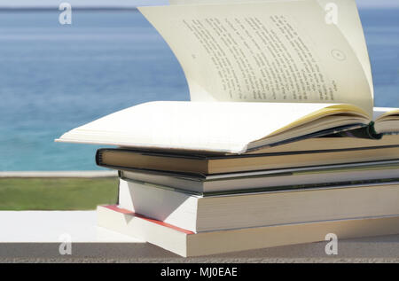 Nur wenige Bücher in senkrechter Linie mit offenem Buch auf die Oberseite und die Seiten drehen sich im Wind und Meer im Hintergrund Stockfoto