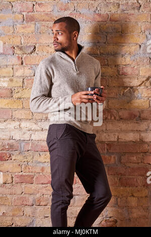 Eine ernsthafte hübscher junger Mann hält eine Tasse in einem Pullover. Stockfoto