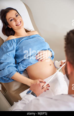 Eine schöne, junge schwangere Frau, Ultraschall durch eine stattliche männliche Arzt scannen. Stockfoto