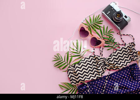 Stilvolle rosa Sonnenbrille, modernen Badeanzug, Foto, Kamera, Kopfhörer und grünen Palmenblättern auf rosa Hintergrund, flach. Platz für Text. Sommer Urlaub Stockfoto