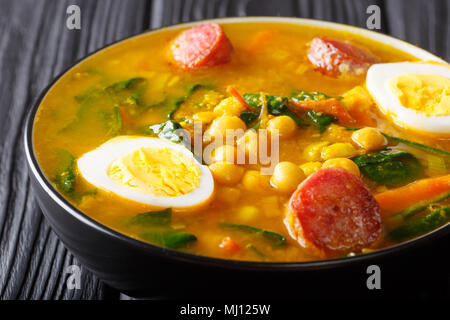 Würzige Suppe mit Spinat, Kichererbsen, Chorizo Wurst, gekochten Eiern close-up in einer Schüssel auf dem Tisch. Horizontale Stockfoto